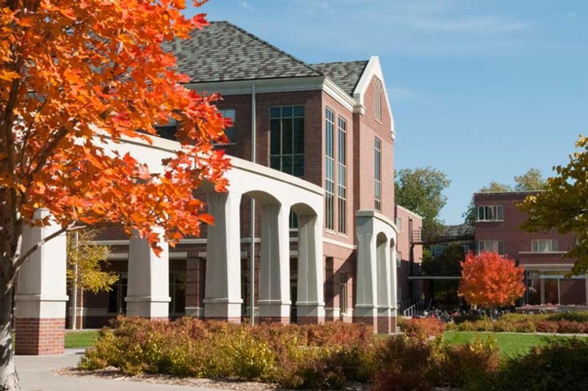 An outdoor photograph of a large brick building with stone arches and shrubberies in front of it.