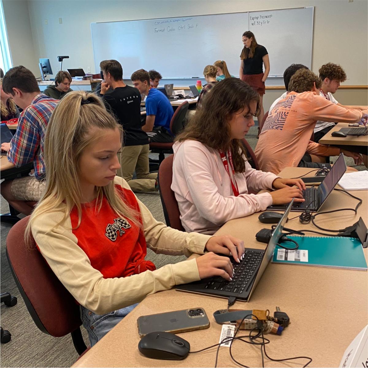 A group of students typing on laptops on a classroom.