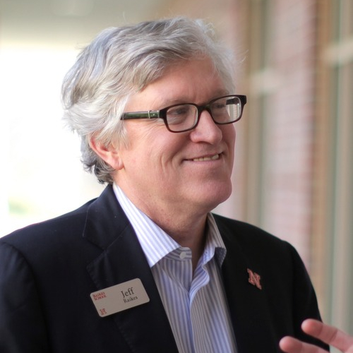 A photo of a man with grey hair and glasses wearing a suit and looking to the right.