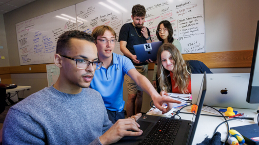 Group of five students looking at notes and a computer screen