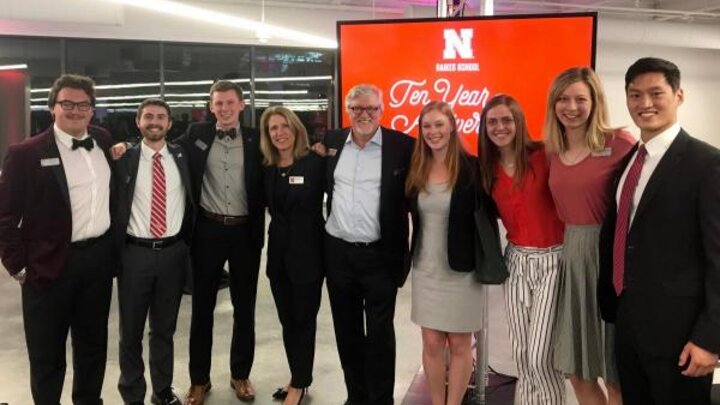 A group of people wearing formal attire gathered for a group photograph in front of a large digital display.