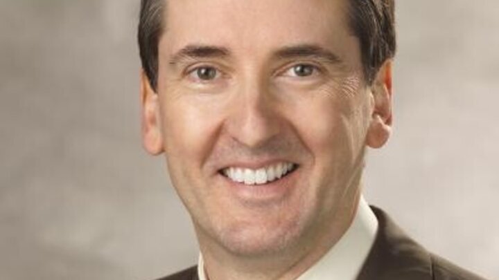 A man wearing a brown blazer with a cream shirt and a patterned tie.