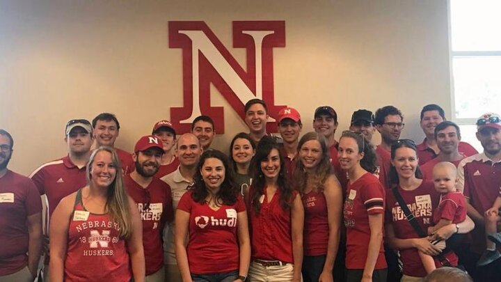 A large group of people wearing red t-shirts standing together in front of a large red and white letter "N" taking a group photograph.