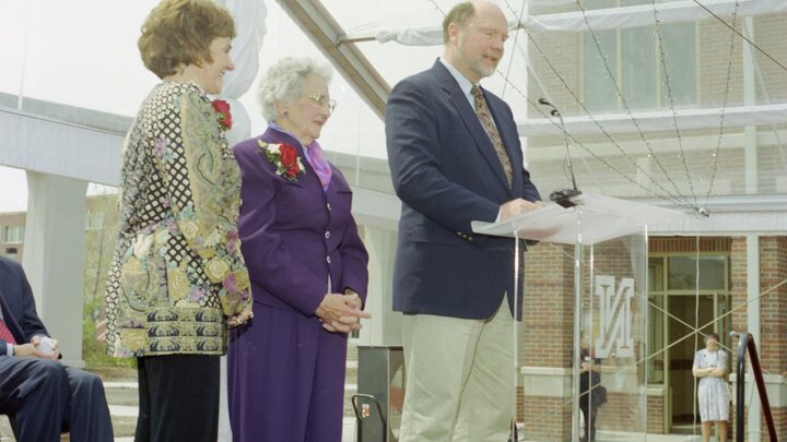 A photograph of three people standing on a stage behind a podium.