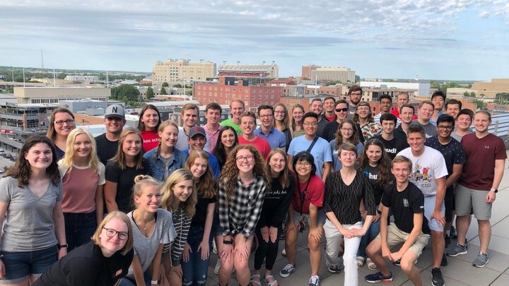 A large group of people gathered on a rooftop for a group photograph with a cityscape in the background.