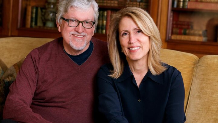 Two people sit closely together on a yellow sofa for a photograph.