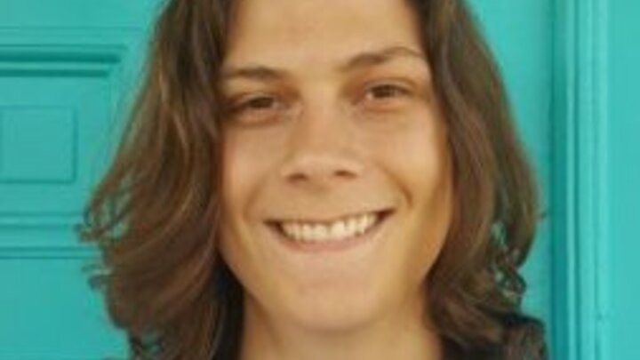 A headshot of a man standing in front of a teal door.