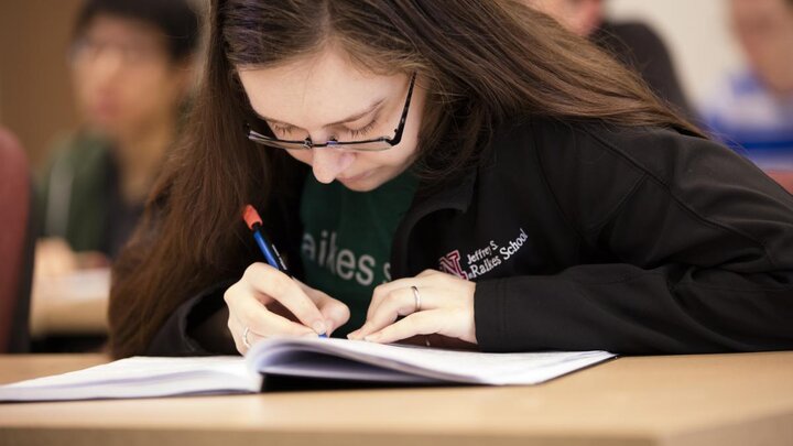 A woman looking down at a desk while writing on a piece of paper.