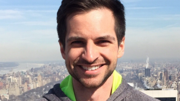 A headshot of a man wearing a grey and green sweatshirt.