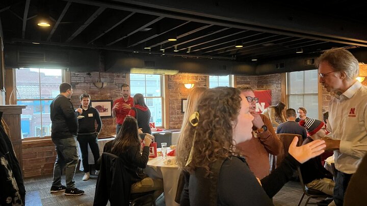 A crowd of people stand in a room and engage in conversations with one another.