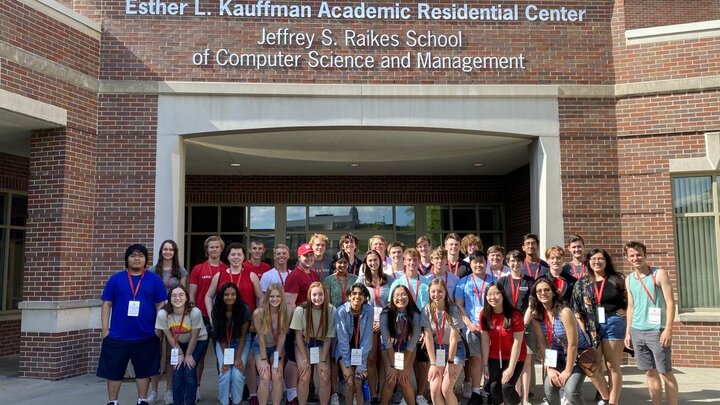 A group of people stand together for a group photograph in front of a large brick building.
