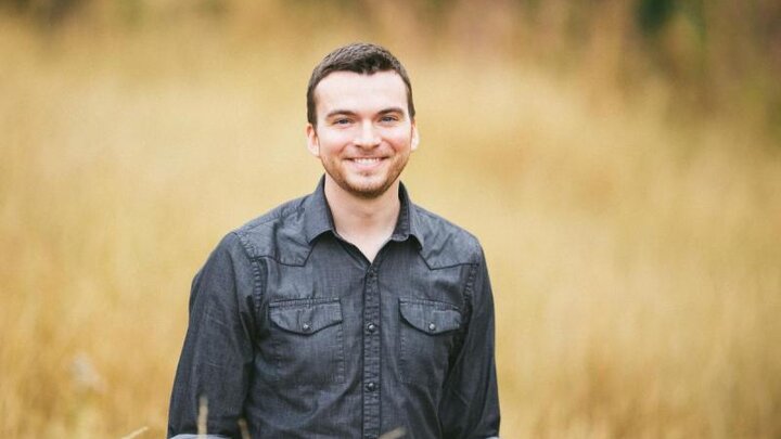 A man wearing a grey shirt stands in a field of wheat.