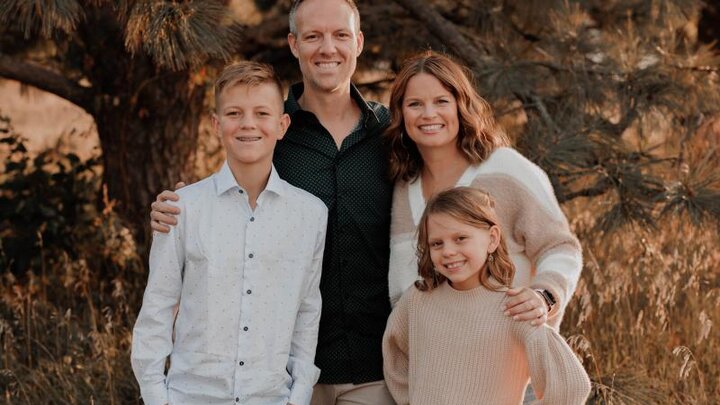 A family stands in front of a tree outdoors for a photograph.