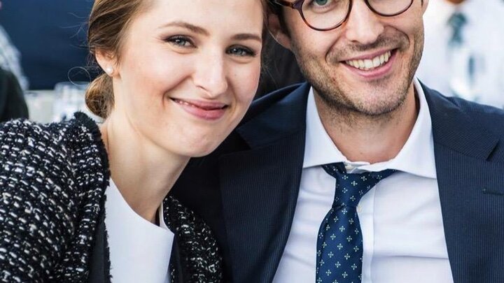 Two people wearing formal attire sit closely together for a photograph.