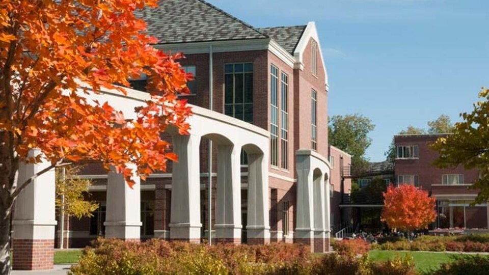 An outdoor photograph of a large brick building with stone arches and shrubberies in front of it.