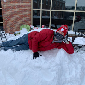 A person lying down on a pile of snow and looking up at the camera.