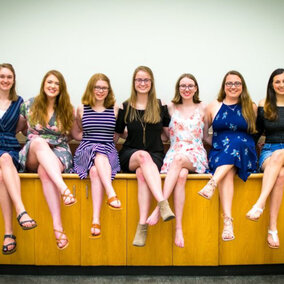 A group of people sat on a long cabinet and facing toward the camera for a group portrait.