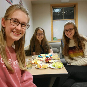 Three people sat around a table with several cut-up apples, looking toward the camera.