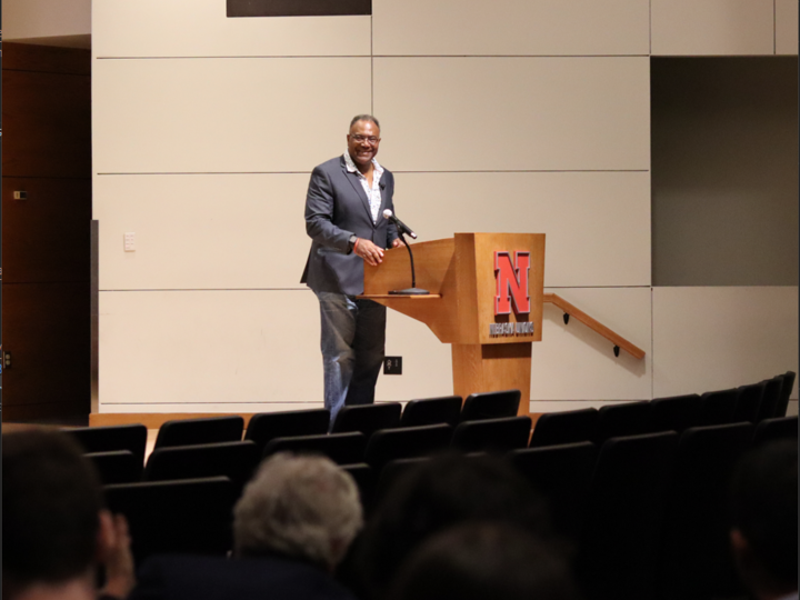 A person standing on a stage behind a podium, speaking out into an audience.