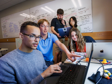 Group of five students looking at notes and a computer screen