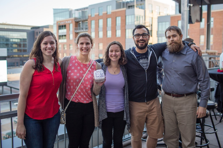 A group of people standing on a balcony with a building in the background taking a group photograph.