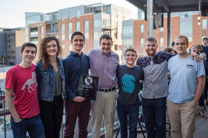 A group of people standing on a balcony with a building in the background taking a group photograph.