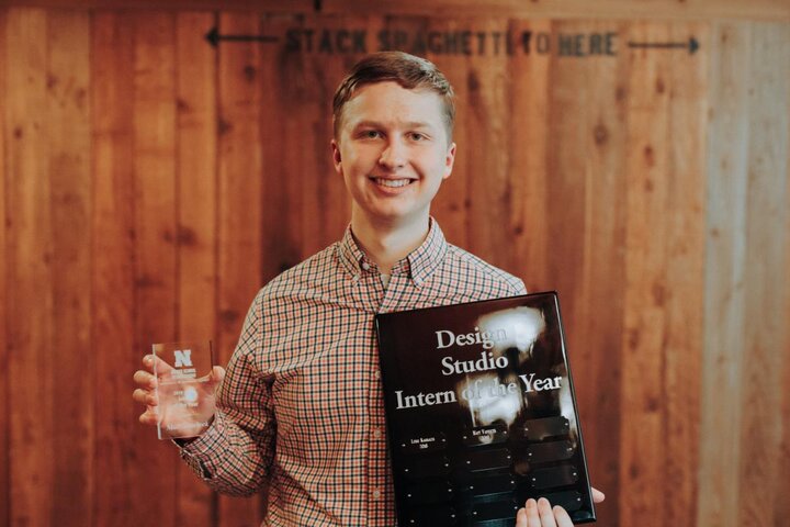 A photograph of a man wearing a checkered shirt, holding up an award.