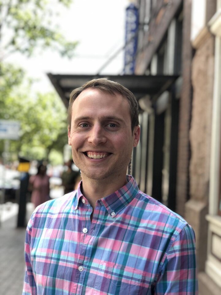 A headshot of a man wearing a blue and pink checkered shirt.