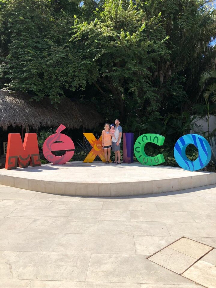 A photograph of two people and a child stood together in front of a large sign.