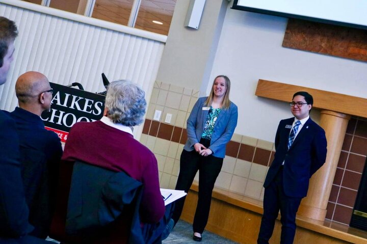 Two people stand together and talk to an audience.