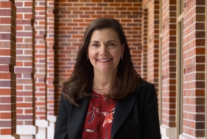 A woman wearing a black suit standing in front of a brick wall.