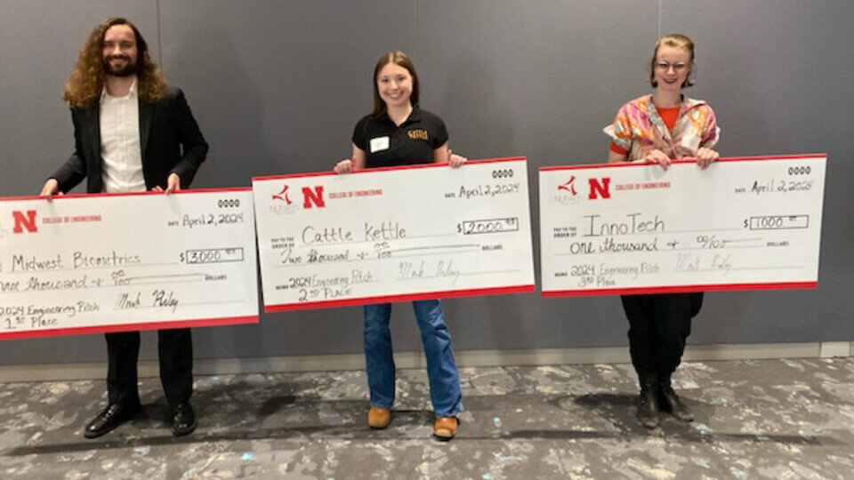 Three people standing in a line, each holding a novelty oversized cheque.