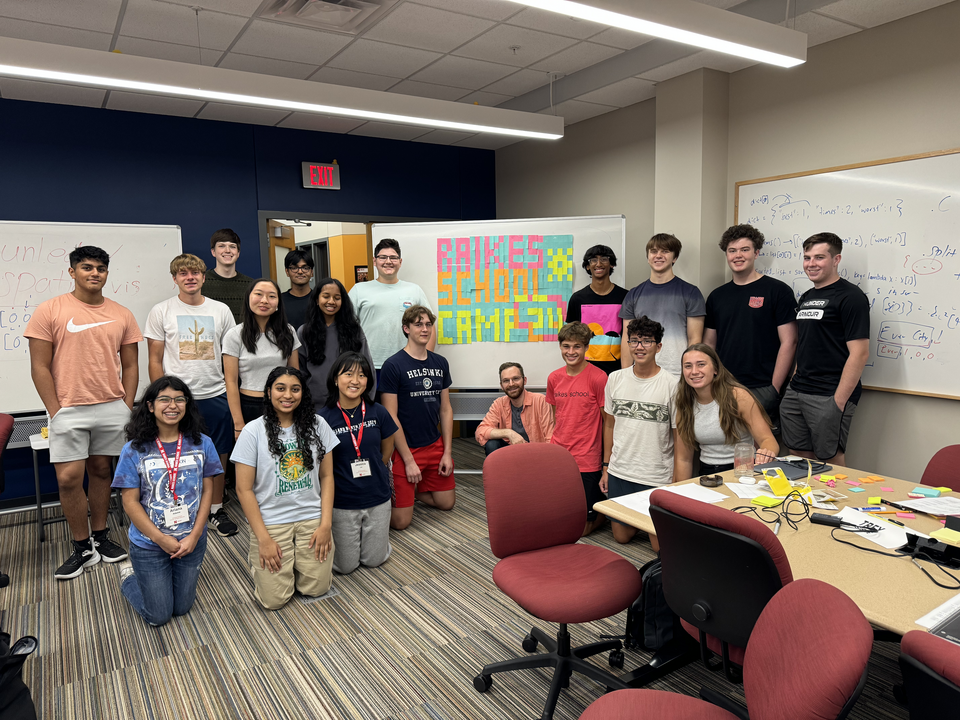 group of students in a classroom posing in front of a whiteboard that says Raikes School Camp