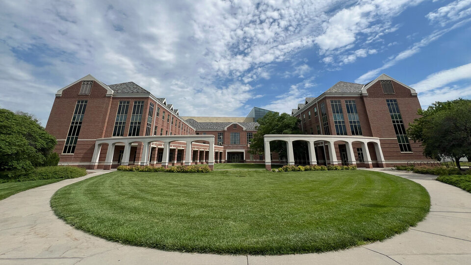 Brick building with arched columns, green lawn, and cloudy blue sky.
