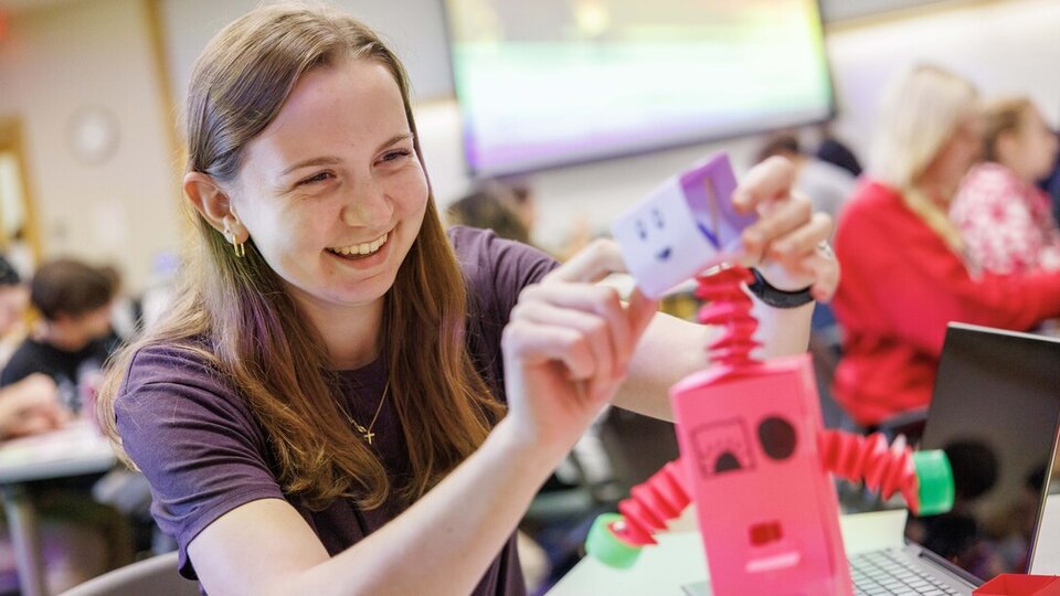 Student assembles a pink robot model in a classroom setting.