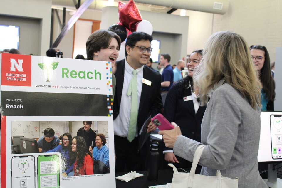 Poster presentation in a design showcase with attendees interacting and colorful balloons in the background.