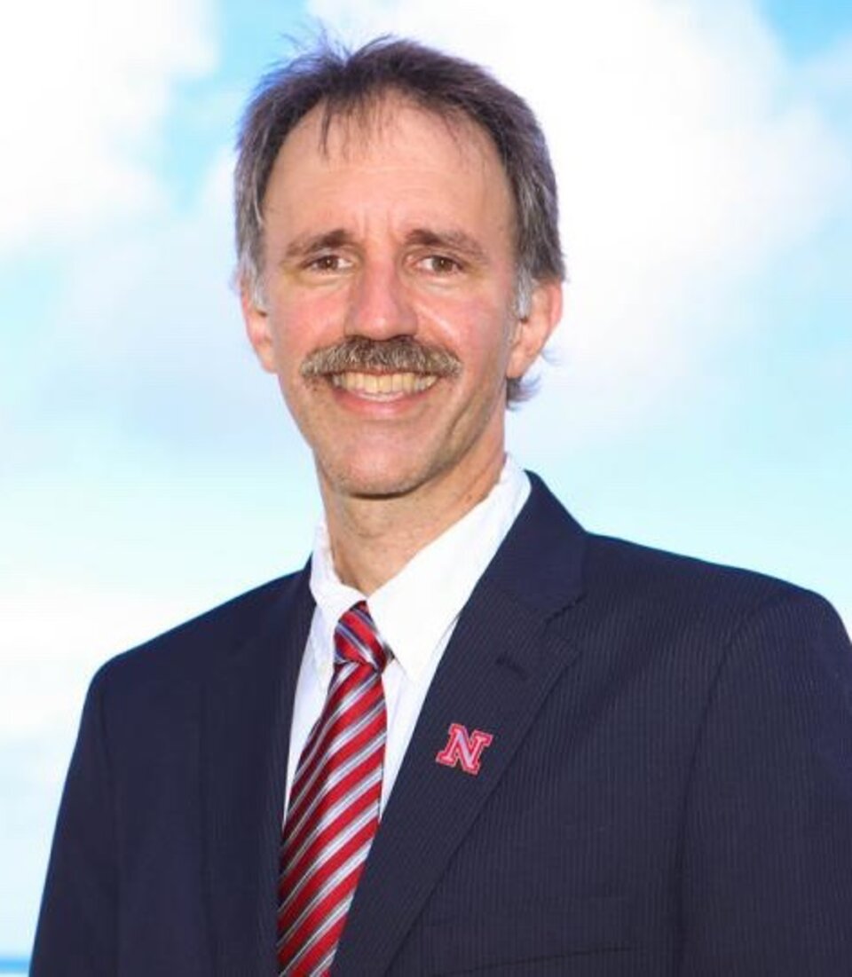 A man wearing a suit with a red tie stood in front of a blue sky