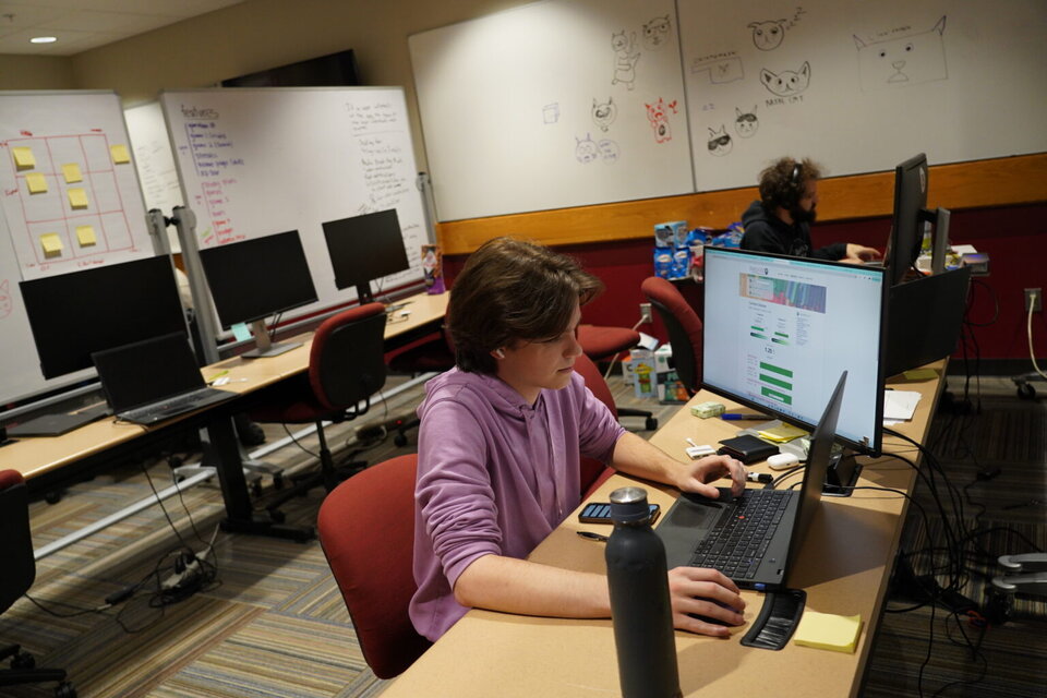 Person working at a desk with computer monitors, in a shared office with whiteboards and sketches.