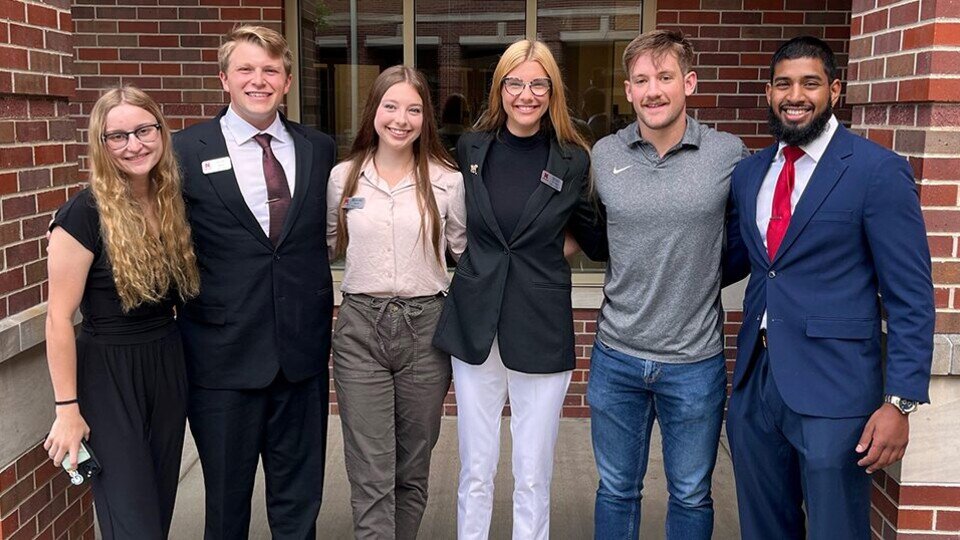 A group of people wearing business attire and standing in front of a brick wall for a group photograph.